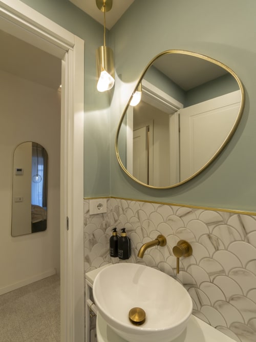 Modern bathroom with gold fixtures, round mirror, and scallop-pattern tile backsplash at YOUnique Boutique Rooms Milano