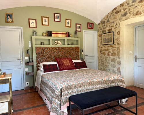 La chambre d'Adrien au Domaine Du Commandeur à Mondragon présente une tête de lit en bois sculpté, une literie à motifs et du charme rustique en pierre