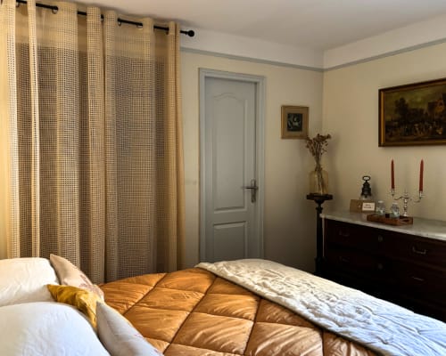 Elegant bedroom at Domaine Du Commandeur B&B in Mondragon with gold quilted bedding, dark wood dresser, and sheer curtains