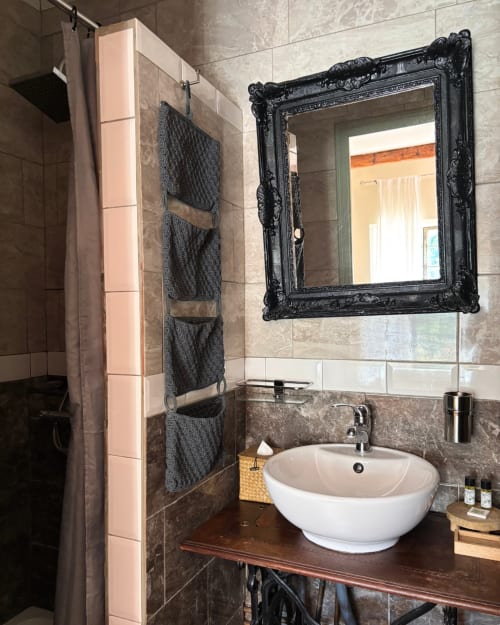 Modern bathroom with round white sink, ornate black mirror, gray tile walls at Domaine Du Commandeur in Mondragon