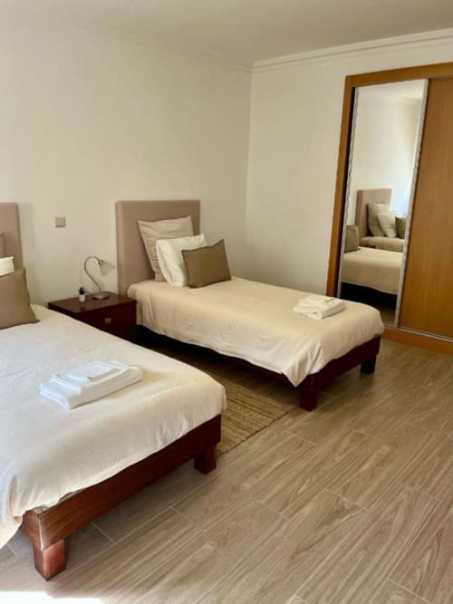 Quarto duplo com roupa de cama creme e cabeceiras estofadas bege na pousada Gomes Equestre Alojamento em Golegã, Portugal