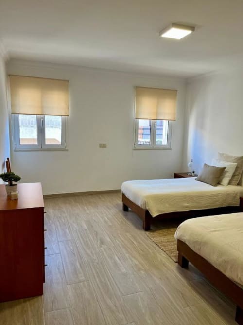 Quarto claro com duas camas, móveis de madeira e janelas na Gomes Equestre Alojamento em Golegã