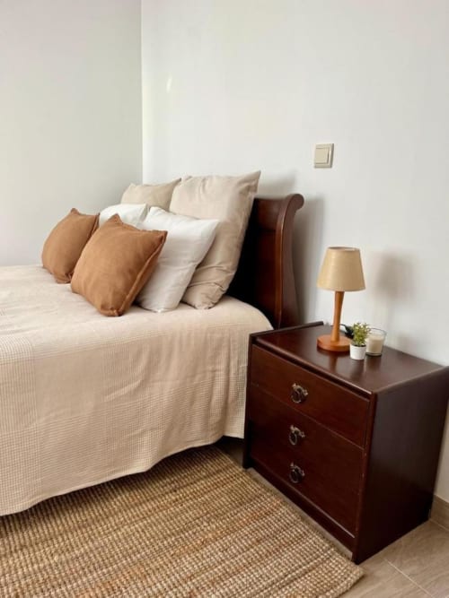 Quarto aconchegante na Gomes Equestre Alojamento em Golegã com cabeceira de couro marrom, roupa de cama creme e criado de madeira