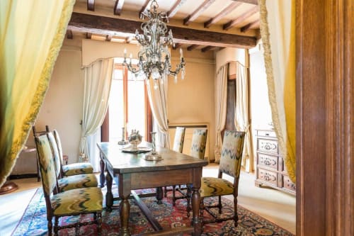 Elegante sala da pranzo della Villa Dom di Piacenza con tavolo in legno scuro, sedie decorate, lampadario in cristallo e travi a vista