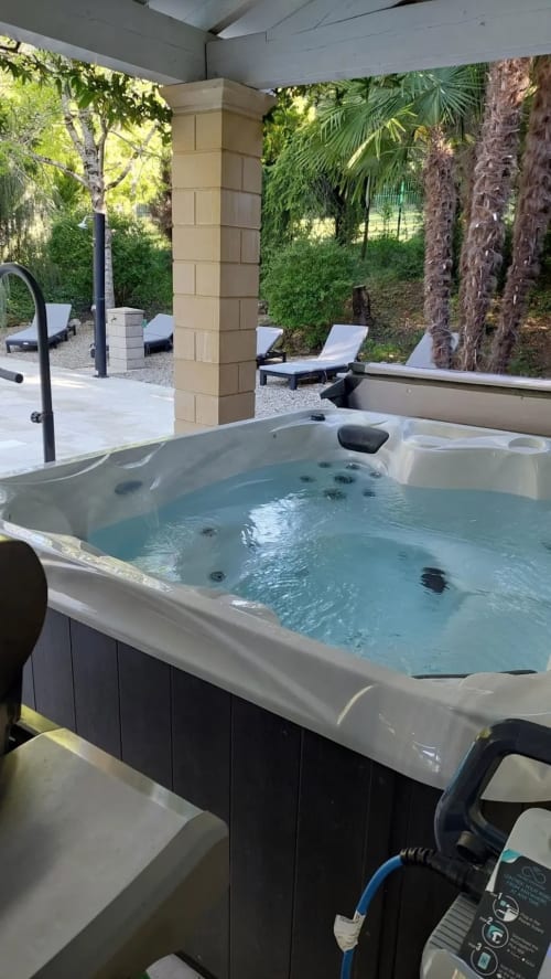 Jacuzzi aux eaux bleues sur terrasse couverte du Domaine de Bize à Mirepoix, vue sur jardin avec transats