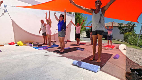 Outdoor yoga class at Corse et Zen with participants in pose under orange shade sails