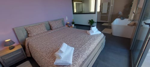 Modern bedroom at Corse et Zen with queen bed, patterned bedding, ensuite bathroom, and ambient purple lighting in Taglio