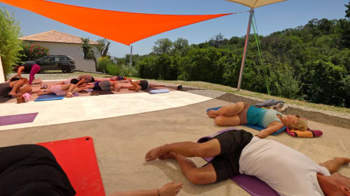 Outdoor yoga class at Corse et Zen, guests practicing on mats under orange shade sail with countryside views