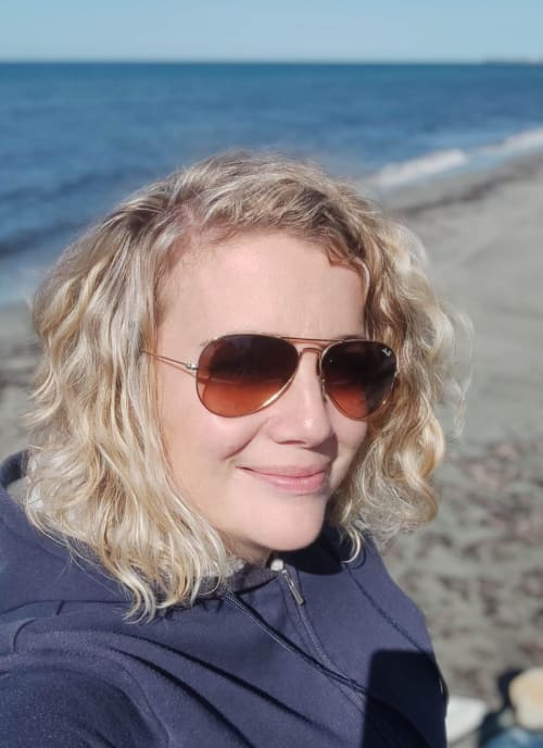 Woman with wavy blonde hair wearing aviator sunglasses at beach near Corse et Zen hotel
