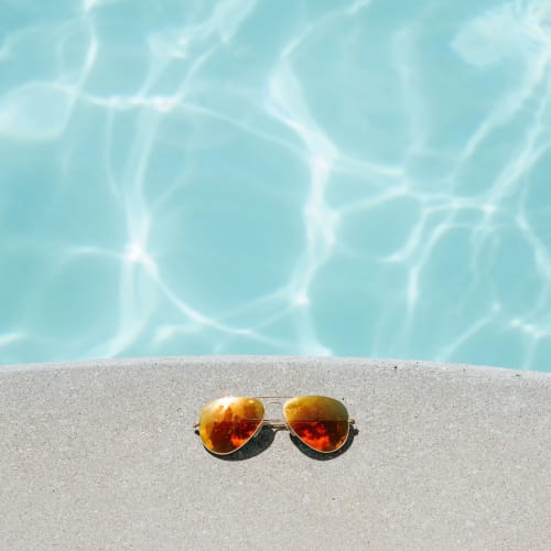 Lunettes de soleil aviateur à monture dorée sur la plage de sable fin face à l'eau turquoise de Corse et Zen, Corse