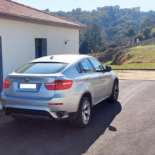 BMW X6 argentée garée à l'hôtel Corse et Zen à Taglio Isolaccio, Corse, avec bâtiment blanc et montagnes boisées en arrière-plan
