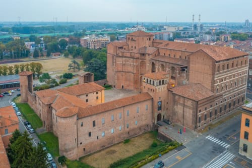 Storica fortezza in mattoni rossi a Piacenza con giardini curati e skyline cittadino sullo sfondo