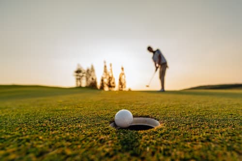 Golfista che mette in buca al campo da golf Villa Dom di Piacenza, con la pallina vicino alla buca e alberi al tramonto