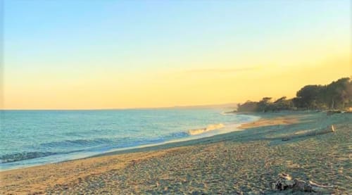 Sunset beach view at Corse et Zen, Taglio Isolaccio, with golden sand, turquoise waters, and coastal cliffs