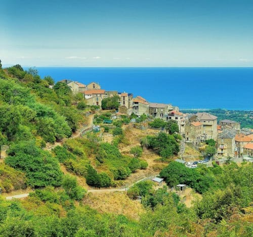 Hilltop village with stone buildings overlooking blue Mediterranean Sea, Corsica