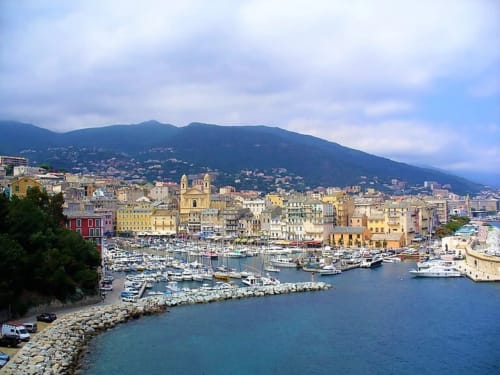 Colorful harbor town with church and boats beneath mountains in Corsica