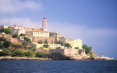 Coastal fortress hotel on rocky island with distinctive pink tower and cream-colored buildings overlooking Mediterranean Sea
