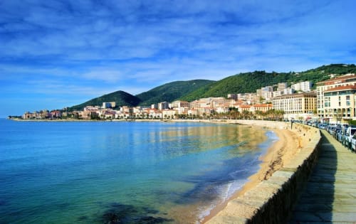 Plage de sable fin aux eaux turquoise cristallines, bâtisses colorées sur les hauteurs, littoral corse à Taglio Isolaccio
