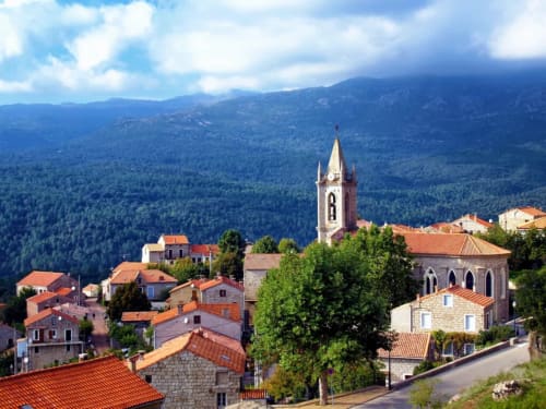 Vue aérienne du village de Taglio Isolaccio avec son clocher, toits en terre cuite et montagnes boisées en Corse