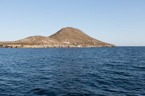 Isla volcánica con laderas marrones en aguas azules del Mediterráneo cerca del destino hotelero Blanca, España