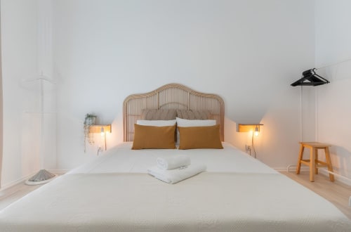 Quarto minimalista luminoso na Galagana Charm House em Golegã com cabeceira de rattan, iluminação aconchegante e detalhes em madeira