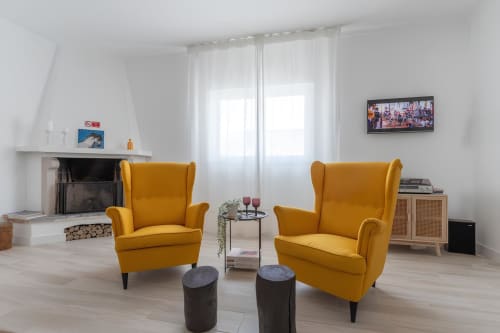 Sala de estar clara e aconchegante na Galagana Charm House com duas poltronas amarelo mostarda, lareira e decoração moderna em Golegã