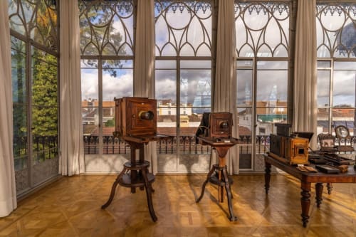 Coleção de câmeras vintage exibida em sala iluminada com janelas ornamentadas com vista para Golegã na Casa de Encanto Galagana
