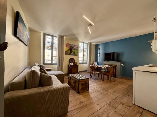 Nowoczesny apartament T2 w Lourdes z pokojem dziennym, zgrabnymi fotelami w paski, meblami z drewna, telewizorem plazmowym i turkusową ścianą akcentową.
