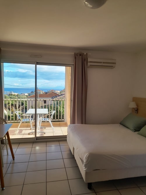Chambre lumineuse de la Résidence Saint Michel avec balcon vue mer, lit et paysage côtier à L'île Rousse