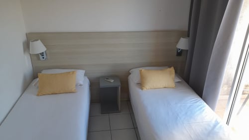 Chambre twin à la Résidence Saint Michel à L'île Rousse avec oreillers jaunes, linge blanc et accès au balcon