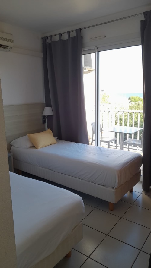 Chambre lumineuse à la Résidence Saint Michel à L'île Rousse avec lit simple, balcon vue mer et rideaux sombres
