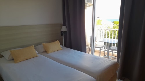 Chambre lumineuse à la Résidence Saint Michel à L'île Rousse avec balcon vue mer, lit double, coussins jaunes et rideaux foncés