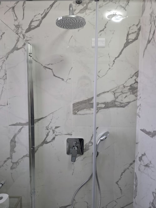 Doccia in marmo moderno con soffione a pioggia e doccetta manuale nell'appartamento THE V Collection a Turate, Italia