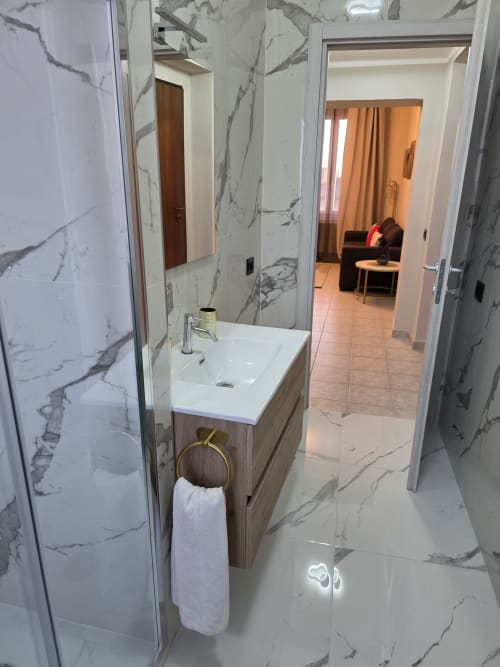 Bagno moderno con pareti in marmo, lavabo bianco e porta asciugamani in ottone nella collezione V