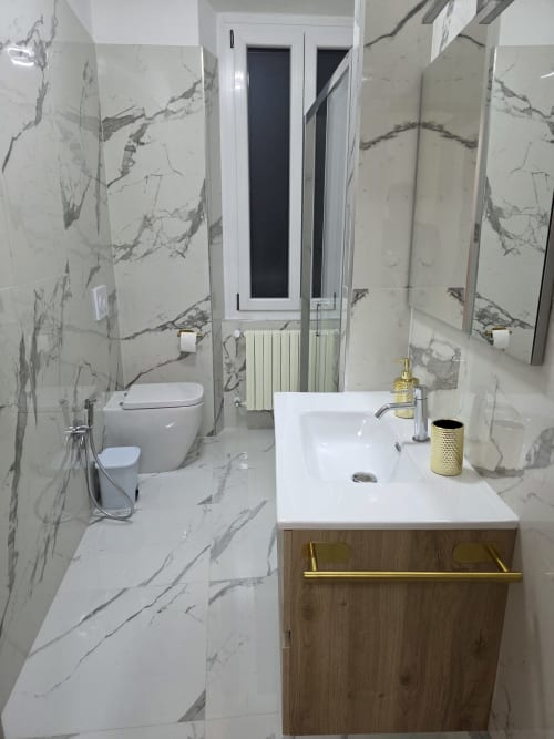 Bagno moderno nell'appartamento THE V Collection Manzoni 1 a Turate con piastrelle effetto marmo, lavabo bianco con dettagli oro
