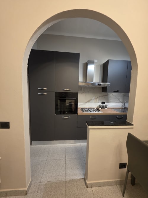 Cucina moderna nera con elettrodomestici in acciaio inossidabile attraverso una porta ad arco nell'appartamento THE V Collection a Turate