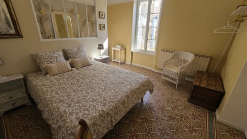 Chambre Béziers au N°9 B&B à Argeliers avec literie à motifs, murs jaunes, vue sur le jardin et fauteuil en rotin