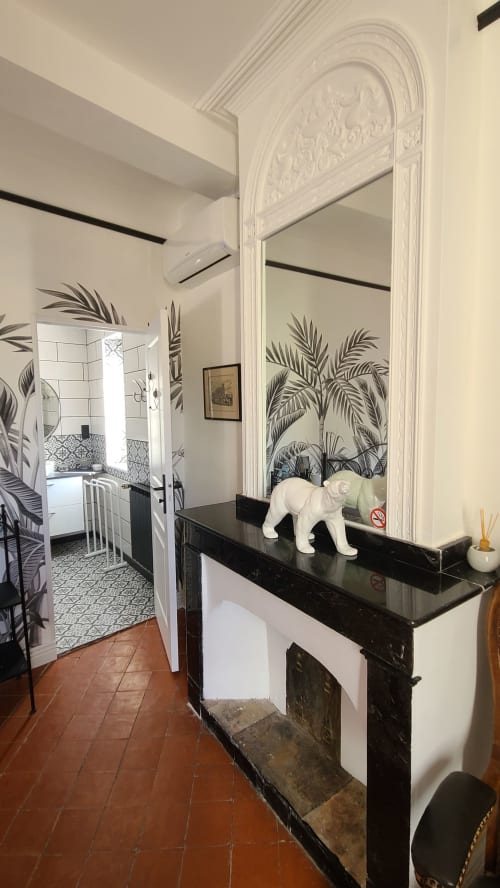 Élégant couloir de la chambre Le N°9 Narbonne avec miroir orné, cheminée noire, sculpture de lion blanc et papier peint feuilles de palmier