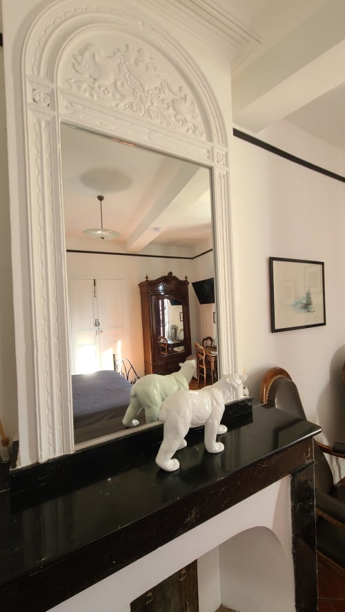 Miroir voûté élégant au cadre blanc orné reflétant la chambre du B&B Le N°9 à Argeliers, avec une figurine de cheval blanc sur fond sombre
