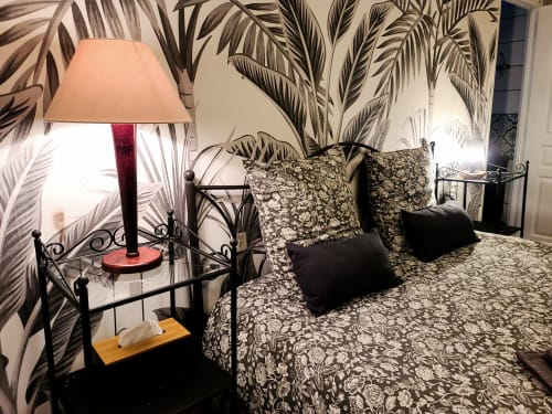 Chambre avec lit en fer forgé, linge de lit à motifs, oreillers noirs, fresque murale tropicale, lampe de chevet, Gîte Le N°9 Argeliers