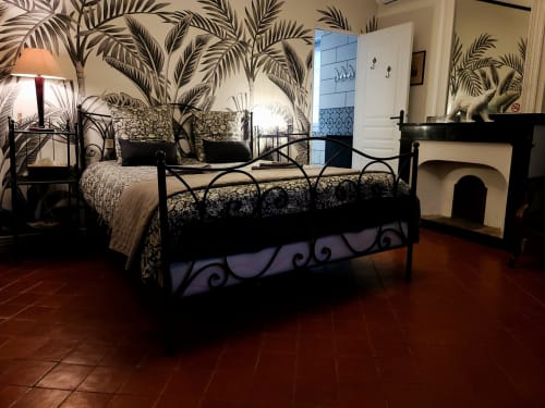Chambre élégante avec lit en fer forgé, papier peint motifs feuilles de palmier et carrelage en terre cuite à Le N°9, guesthouse à Argeliers, France