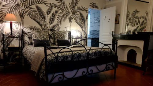 Chambre élégante avec lit en fer forgé, papier peint tropical, cheminée et vue sur la ville au boutique B&B Le N°9 à Argeliers