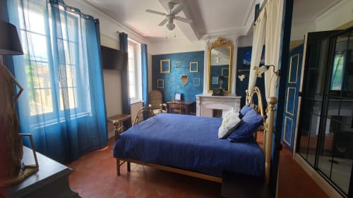 Chambre élégante au N°9 B&B à Argeliers avec lit en laiton à cadre bleu, mur d'accent bleu, cheminée et vue sur la ville