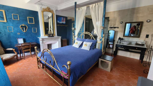 Chambre Gruissan au N°9 d'Argeliers avec murs bleu acier, lit en laiton, cheminée et carrelage en terre cuite