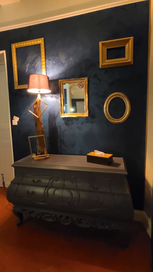Présentoir élégant au N°9 Argeliers avec mur sombre, cadres dorés, lampe décorative et base vintage en valise