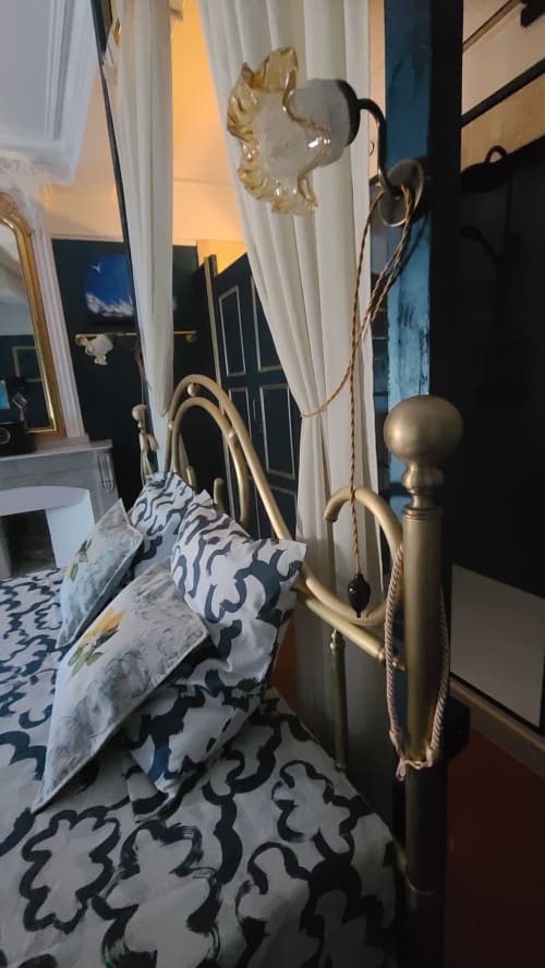 Chambre élégante au N°9 d'Argeliers avec lit doré, coussins à motifs, voilages fins et vue sur la ville