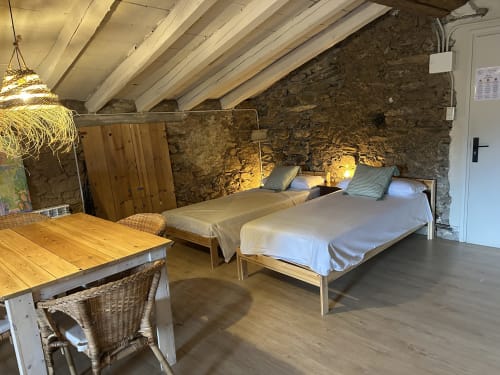 Dormitorio rústico de piedra en Casa Tapiolas en Molló con vigas de madera, dos camas, zona de comedor y vistas a la montaña