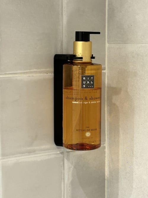 Dispensador de champú y gel de ducha de lujo montado en la pared de baño con azulejos blancos del hotel de montaña Casa Tapiolas en Molló, Girona