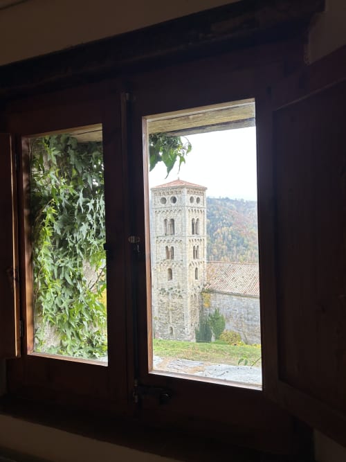 Vista desde la habitación Casa Tapiolas a través de puertas abiertas hacia la torre campanario medieval de piedra y las montañas de Girona