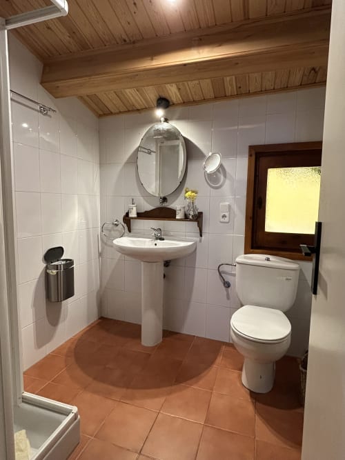 Baño moderno en Casa Tapiolas en Molló, Girona con azulejos blancos, lavamanos de pedestal, inodoro y suelo de barro